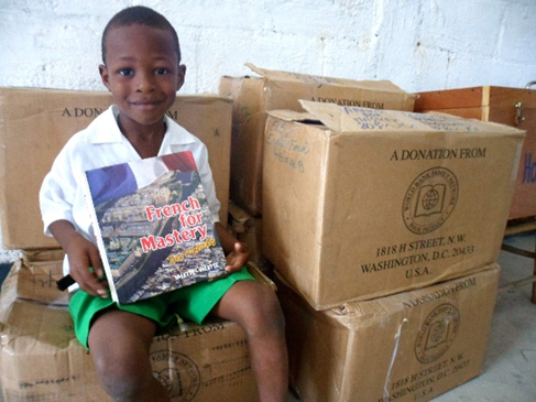 A boy in Haiti sitting among boxes of schoolbooks from the WBFN Book Project